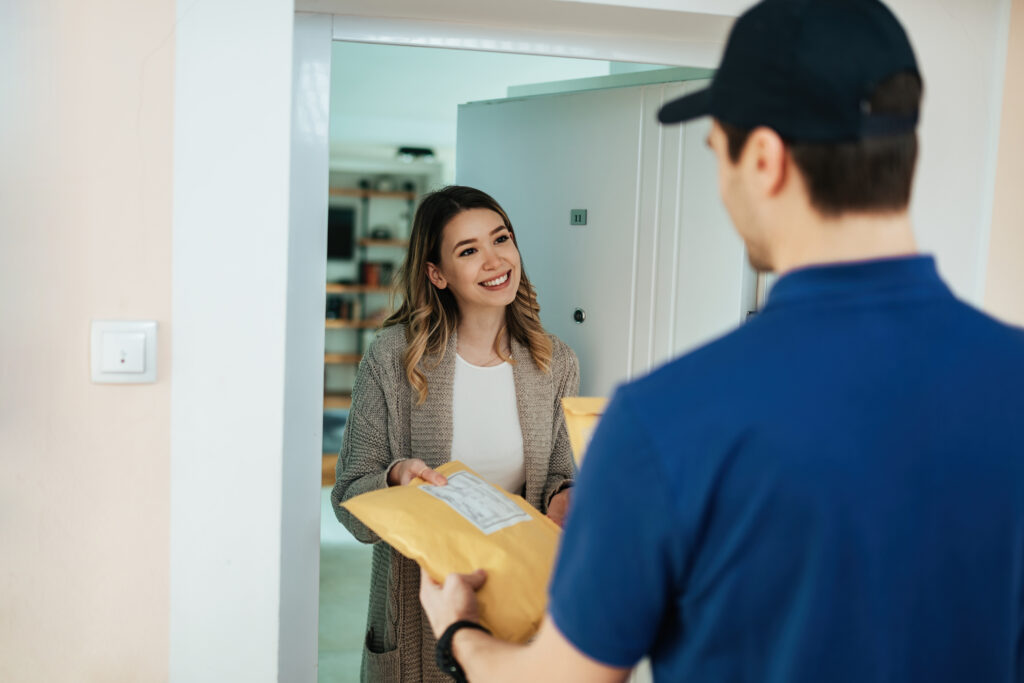 A courier handing a parcel to a smiling woman at her front door.