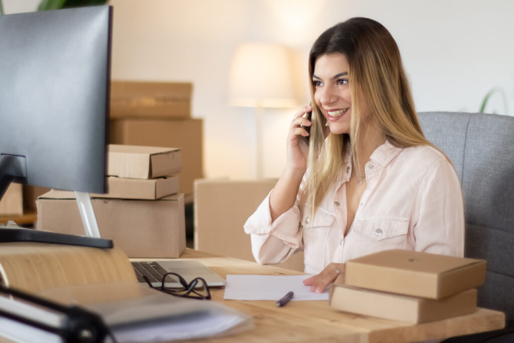 A smiling woman on the phone at her desk, surrounded by small parcels.